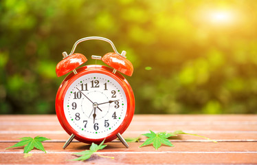 Morning concept. Alarm clock closeup. Red alarm clock on garden table with natural lights background, outdoors