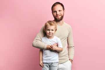 happy father and his kid posing to the camera. close up portrait, isolated pink background, studio shot