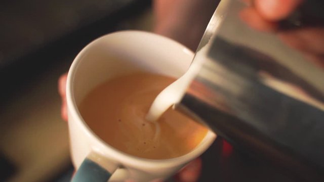 Slow motion of barista pouring milk over coffee creating a perfect cappuccino or latte