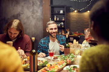 Portrait of modern adult man smiling happily while enjoying dinner with friends sitting a table in dimly lit room, copy space