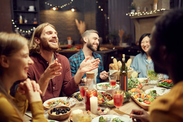 Group of emotional young people enjoying dinner party with friends and smiling happily sitting at table in dimly lit room, copy space - Powered by Adobe