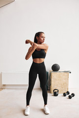 Slim fitness female in black leggins and topic stretching body, arms. White gym background