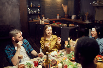 Multi-ethnic group of young people playing guessing game while sitting at table during dinner party...