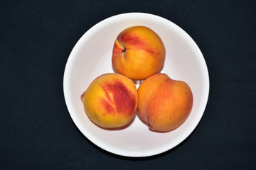 Isolated closeup of 3 three ripe peaches in a white bowl on a black background