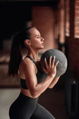 Gardinen Slim flexible female in black sportswear do exercises in fitness gym. Brickwall background © alfa27