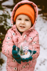 Child hold transparent glass ball with christmas tree and house inside.