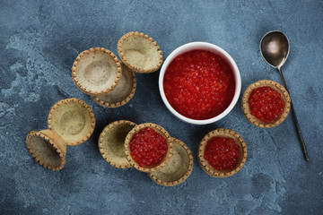 Bowl of red caviar and tartlets on a blue stone background, flatlay, horizontal shot
