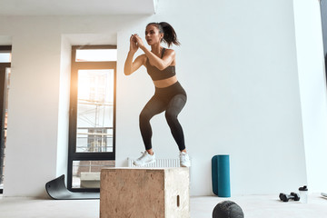 Beautiful sporty woman in sportswear jumping on wooden box in gym. Training, cross fit, sport - obrazy, fototapety, plakaty