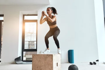 Gardinen Beautiful sporty woman in sportswear jumping on wooden box in gym. Training, cross fit, sport © alfa27