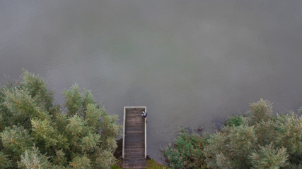 Autumn mood at the lake. Woman with warm clothes on a dock at a lake.Drone view.