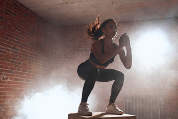 Fototapeta na wymiar Beautiful sporty woman in sportswear jumping on wooden box in gym. Training, cross fit, sport