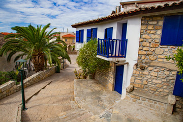 Fototapeta na wymiar Greece. Street of the resort. A picturesque house with blue shutters. Rest in a small town. Pastoral landscape. Summer trip to Greece. Mediterranean.