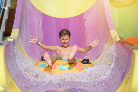 Cute boy sliding on floater down slide in waterpark. He enjoying his summer vacations. His hands are wide open.