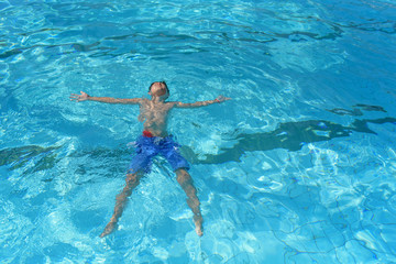 Healthy lifestyle. European boy in blue swim shorts swimming in the blue clear sea water during his trip to Spain.