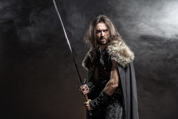 Man dressed in medieval armor and raincoat with longs word fighting against enemy. Courage fantasy warrior knight with long hair concept historical photo - 295640909
