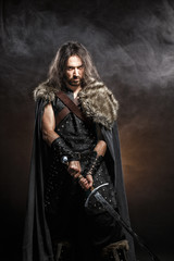 Man dressed in medieval armor and raincoat with longs word fighting against enemy. Courage fantasy warrior knight with long hair concept historical photo