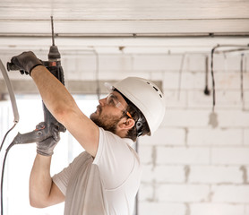 Handyman uses jackhammer, for installation, professional worker on the construction site. The concept of electrician and handyman.