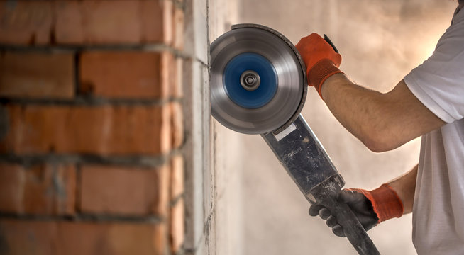 The industrial Builder works with a professional angle grinder to cut bricks and build interior walls. Electrician.