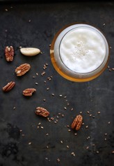 Obraz na płótnie Canvas flat lay photo of pale beer in glass on dark gray background with some pecans sesame seeds and brazil nut