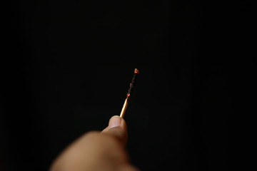 Burnt extinguished match held in hand on black rugged background.