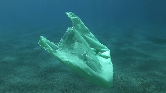 Slow motion, old green plastic bag drifts slowly under surface of the blue water. Underwater plastic pollution of the oceans. Plastic garbage environmental pollution problem