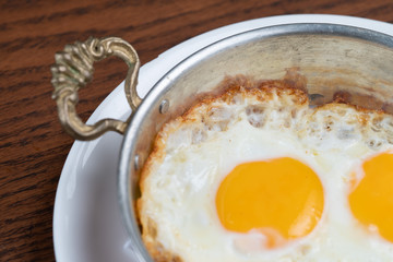 Closeup of fried egg in copper pan isolated on wooden table