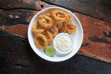 Top view of fried calamari rings with dip sauce isolated on rustic wooden table