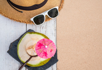 Fresh coconut drink and summer accessories, sunglasses, hat on white wood table at sand beach