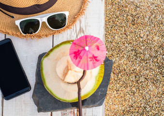 Fresh coconut drink and summer accessories, sunglasses, hat, mobile phone on white wood table