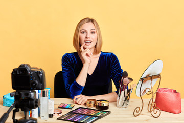 Portrait of curious pretty blogger girl going to record new beauty podcast, making review on cosmetics, holding her chin thoughtfully, index finger near her open mouth, wearing orthodontic braces.