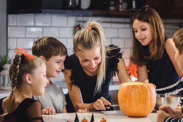 Mother carving Halloween pumpkin with children at decorated home kitchen