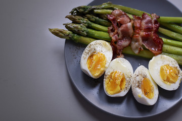 Healthy breakfast - green asparagus wrapped with bacon, boiled egg. Breakfast on a blue table closeup.