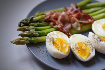 Healthy breakfast - green asparagus wrapped with bacon, boiled egg. Breakfast on a blue table closeup.