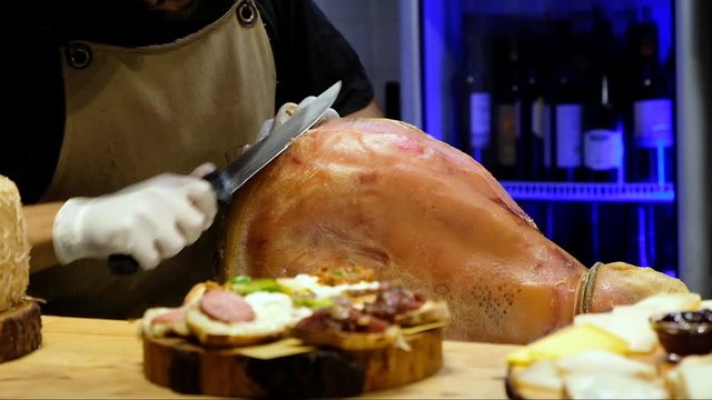senior chef utting jamon prosciutto ham in a restaurant, italian or spanish cuisine
