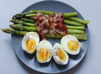 Healthy breakfast - green asparagus wrapped with bacon, boiled egg. Breakfast on a blue table closeup.