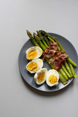 Healthy breakfast - green asparagus wrapped with bacon, boiled egg. Breakfast on a blue table closeup.