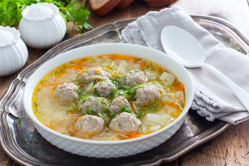 Homemade soup with meatballs and noodles in a white plate on a metal tray, selective focus