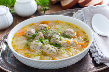Homemade soup with meatballs and noodles in a white plate on a metal tray, selective focus