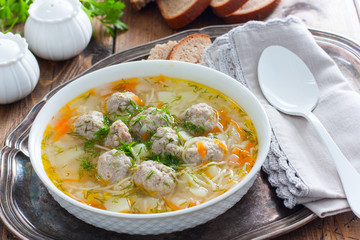 Homemade soup with meatballs and noodles in a white plate on a metal tray, selective focus