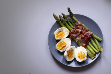 Healthy breakfast - green asparagus wrapped with bacon, boiled egg. Breakfast on a blue table closeup.