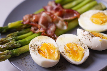 Healthy breakfast - green asparagus wrapped with bacon, boiled egg. Breakfast on a blue table closeup.