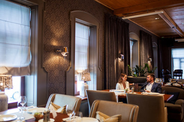 Close up of beautiful young couple with glasses of white wine sitting in cozy soft chairs in luxury restaurant