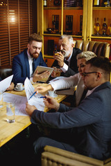 Businesswoman showing pencil on paper. Businessman in glasses listening to explanations and takes notes. Red head bearded man showing presentation on laptop to chief man, side view