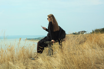 A young woman looks at the screen of a smartphone and photographs the landscape.