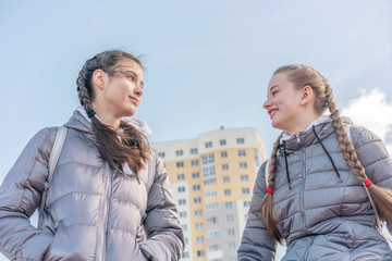 girlfriends teenagers with pigtails in warm gray jackets talking walk on street outdoor