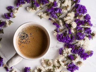 Delicious morning ceramic white cup of coffee with dry white and violet flowers on the light...