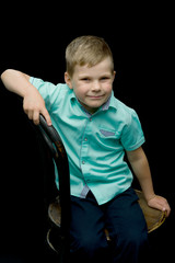 Smiling little boy sitting on stool, on a black background.