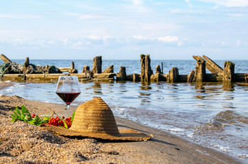 A great picnic by the sea with red wine in a glass, a hat and berries.