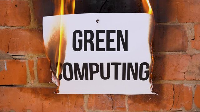 The inscription on a white A4 size sheet against the background of an orange brick wall. The paper with the black word Green Computing burns, smoke and turns into ashes. Business concept.