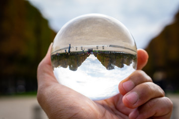 Crystal ball used as telling object. Sperical transparant glass. Paris park in the background with fall or autumn trees color